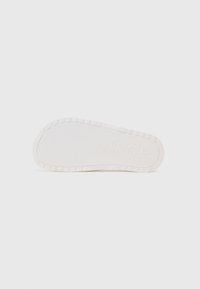 Witte rubberen schoenzool met een gestructureerd oppervlak en geribbelde randen. Bevat reliëf branding en een glad centraal gebied voor comfort.