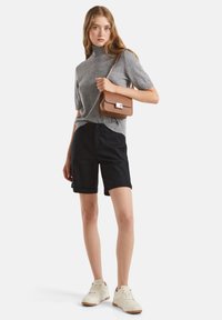 Šedý krátký rukávový rolák, černé šortky po kolena, světlé tenisky a malá hnědá crossbody taška s kovovými akcenty.