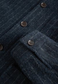 Donkerblauwe wollen stof met ribbeltextuur, voorzien van een knoopmanchet en donkere ronde knopen op een kledingstuk.