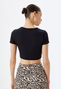 Sort cropped t-shirt lavet af glat stof, med korte ærmer og rund halsudskæring, parret med leopardmønstrede højhuskede bukser.