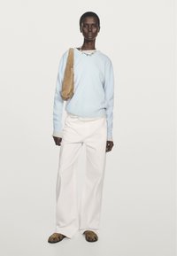 Ljusblå tröja, vita vida byxor och brun mockaväska. Svarta platta sandaler med djurmönstrade detaljer. Enkel halsband.