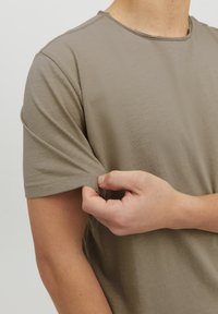 Camiseta verde olivo con cuello redondo, mangas cortas y un corte relajado. La tela parece suave con una textura sutil y detalles de costura visibles.
