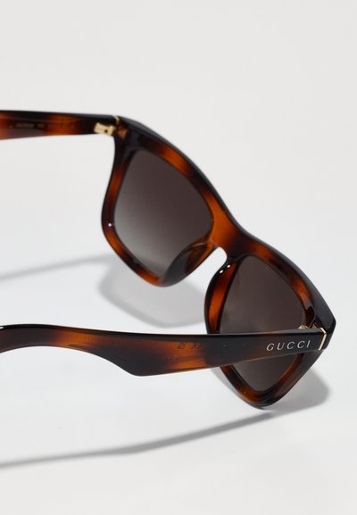 Gucci solbriller med en skildpadde-agtig ramme, mørke linser, vinkelret design og guldfarvet detalje på templet med logo graveret.