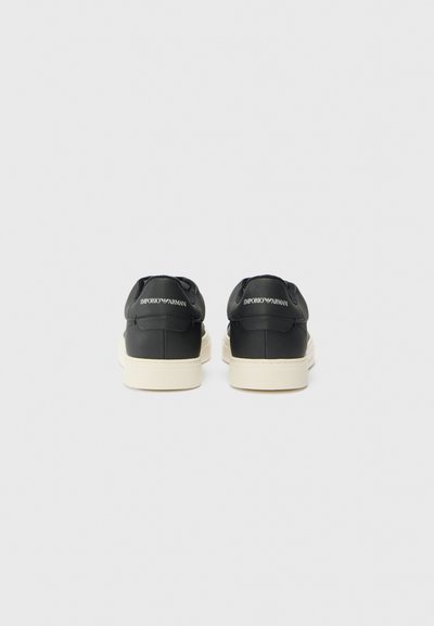 Black leather sneakers with a white rubber sole, featuring a low profile and embossed logo detail on the rear heel.