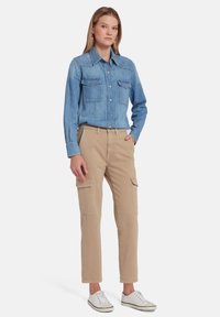 Lichtblauwe denim overhemd met twee borstzakken, gecombineerd met beige cargobroek met zijzakken en witte sneakers. Eenvoudig, casual ontwerp.
