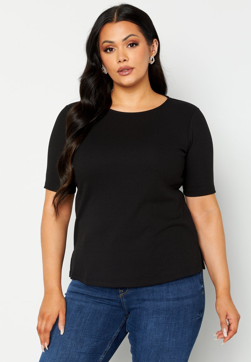 Top corto nero a coste con scollo tondo, caratterizzato da un taglio dritto e spacchi laterali. Abbinato a jeans di denim blu.