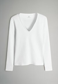 Top bianco a maniche lunghe con scollo a V, caratterizzato da una texture a costine e una vestibilità comoda, con spacchi laterali sull'orlo per un tocco di originalità.