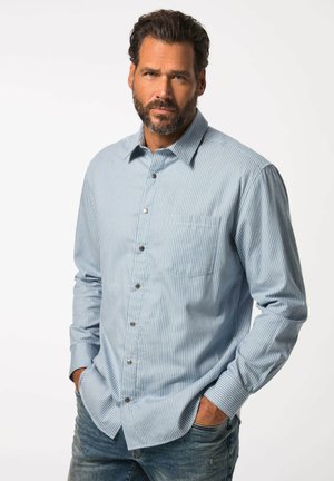 Helles blau gestreiftes Hemd mit langen Ärmeln, einer Brusttasche auf der linken Seite und silbernen Knöpfen. Getragen über verblichenen blauen Jeans.