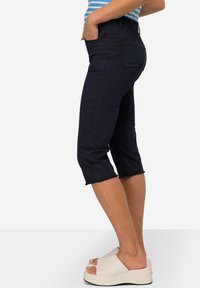 Jean capri marine à coupe slim, avec un ourlet délavé et des poches latérales, associés à des sandales à plateforme beiges avec une large bride.