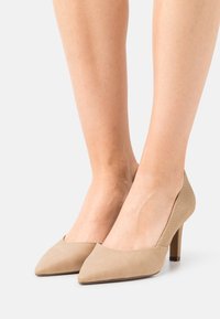 Escarpins beiges à talons hauts avec un design à bout pointu. Fabriqués en daim texturé, avec une section avant lisse et un talon texturé.