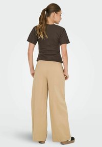 Brun kortærmet t-shirt parret med beige brede bukser, der har en afslappet pasform og glat stof tekstur. Bagview vist.