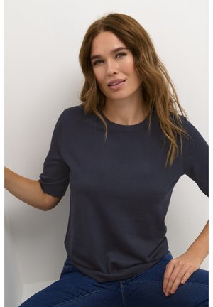 Dark navy short-sleeve sweater in soft, smooth fabric. Round neckline, relaxed fit, slightly rolled sleeves, paired with blue jeans.
