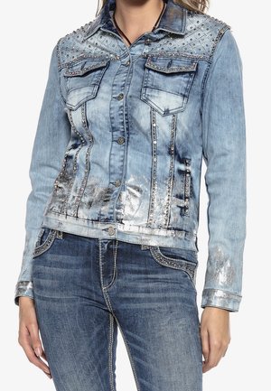 Lyseblå denimjakke med sølvudsmykning og rhinsten på skuldre, for- og sidesømme samt manchetter, båret med matchende mørkeblå jeans.