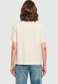 Cream short-sleeve t-shirt with a relaxed fit, made of soft cotton, featuring a simple design and a straight hem, paired with light blue jeans.