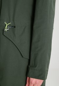 Olivgrön, lätt jacka med rundad krage, justerbar dragsko och en tygetikett med varumärkets namn. Slät textur och skräddarsydd passform.