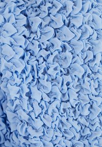 Světle modrý látkový materiál s texturovaným, rýhovaným povrchem, který má nepravidelné záhyby a vrásky po celém povrchu. Materiál vypadá jemně a lehce.