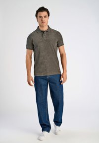 Donkergrijze polo met korte mouwen en een gestructureerde afwerking, gecombineerd met losse blauwe denim jeans en witte sneakers.
