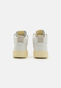 Vysoké tenisky vyrobené z bílé kůže s béžovými akcenty, vybavené polstrovanými límci a texturovanými gumovými podešvemi.