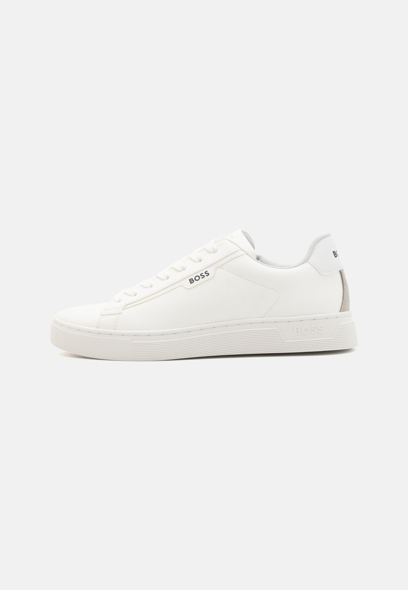 Baskets blanches en cuir avec une texture lisse, bout rond et semelle plate. Présente un logo de marque discret sur le côté et une languette de talon grise contrastante.