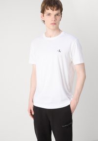 Λευκό βαμβακερό μπλουζάκι με στρογγυλή λαιμόκοψη και κοντά μανίκια, με μικρό μαύρο λογότυπο στο αριστερό στήθος και χαλαρή εφαρμογή.