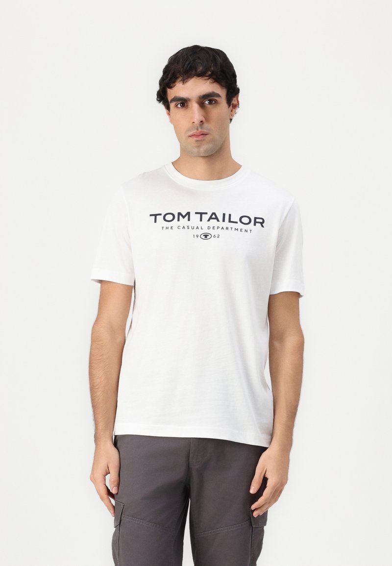 Hvid bomulds t-shirt med korte ærmer, der har et sort trykt logo "TOM TAILOR" foran. Rund halsudskæring, afslappet pasform.