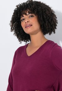 Langarm-Top mit V-Ausschnitt in tiefem Burgunderrot, aus weichem, strukturiertem Stoff hergestellt. Verfügt über eine entspannte Passform und minimale Nähte.