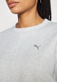 Sudadera gris clara con cuello redondo, que presenta un pequeño logo de Puma en gris oscuro en el pecho y un acabado de tela texturizada.