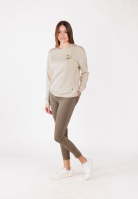 Felpa beige con un patch floreale, abbinata a pantaloni skinny verde oliva e sneakers bianche. Tessuto morbido e vestibilità comoda.