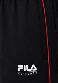 Μαύρο ύφασμα με λευκό λογότυπο FILA Smilodox κοντά σε κάθετή τσέπη που περιβάλλεται από μια λεπτή κόκκινη γραμμή.