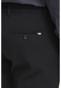 Czarne spodnie z gładkiego materiału mają zapięcie na guzik i tylną kieszeń z paskowym akcentem. Projekt jest dopasowany i elegancki.