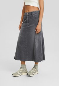 Falda maxi de mezclilla gris con cintura ajustada, parte inferior acampanada y dobladillo sin rematar. Combinada con zapatillas deportivas beige y calcetines gris claro.