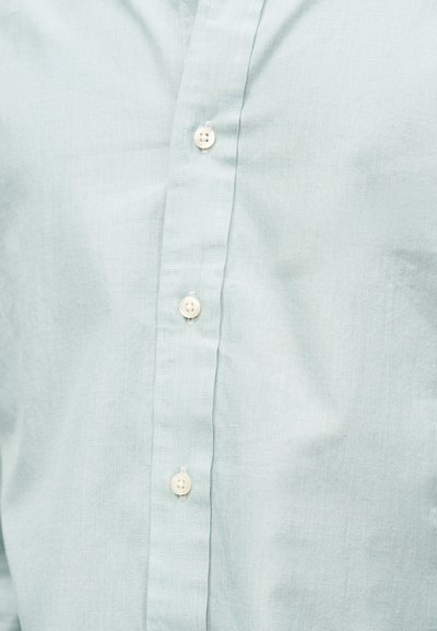 Lyseblå bomullsskjorte foran med fire hvite knapper og sydd stolpelukkingsdetalj.