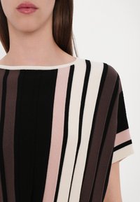 Stickad topp med breda ränder i svart, mörkbrun, ljusrosa och krämfärgad. Har en rundad halsringning och avslappnad passform. Mjuk textur.