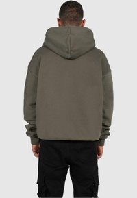 Felpa over-size verde oliva con un ampio cappuccio, polsini a coste e orlo dritto. Tessuto liscio e vestibilità facile, indossata con pantaloni cargo neri.