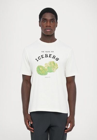 Weißes Baumwoll-T-Shirt mit grafischem Druck von grünem Eisberg-Salat und schwarzem Text "DER GESCHMACK FÜR EISBERG" mit "Seit 1974" darunter.