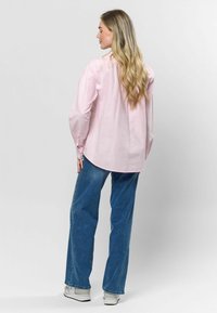 Světle růžová košile s dlouhými rukávy, volný střih a zaobleným lemem, spárovaná s modrými kalhotami širokého střihu a bílými teniskami.