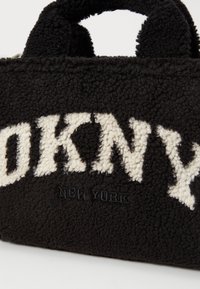 Sac à main en tissu noir texturé avec des lettres blanches "DKNY" et un texte plus petit "New York" en dessous sur le devant.