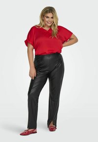 Röd satinblus med V-ringning, i kombination med svarta byxor i konstläder med en mjuk textur och sidosprund. Röda dekorerade lägenheter.