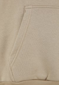 Beige sweatshirts stof med en kænguru-lomme, der har synlige syningsdetaljer. Glat tekstur og ribbet talje i bunden.