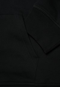 Felpa con cappuccio nera in cotone, con polsini a costine, tasca a marsupio frontale e cuciture piatte. Texture morbida, design pulito, senza pattern.