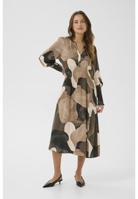 Ilga suknelė su V formos iškirpte, puošta abstrakčiais raštais žemės tonais – juodos, smėlinės ir žalios spalvos. Pagaminta iš lengvos medžiagos su suploto liemens dizainu.