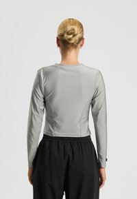 Light grey long-sleeve top with a fitted design, smooth texture, round neckline, and seam detailing. Paired with black elastic waistband pants.