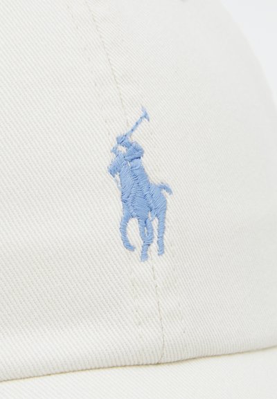 Căciulă din bumbac de culoare crem, având un logo brodat cu un jucător de polo în nuanță de albastru deschis. Include un material texturat și cusături cusute.