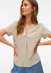 Haut beige à manches courtes avec des rayures verticales bleu marine, décolleté en V et coupe décontractée. Un matériau doux et un ourlet droit caractérisent le design.