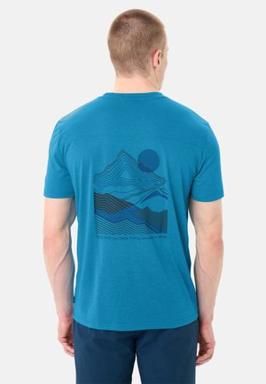 Mann trägt blaues T-Shirt mit Berg- und Sonnenmotiv und dem Text "TOGETHER_out there, finding new paths in nature" auf dem Rücken.