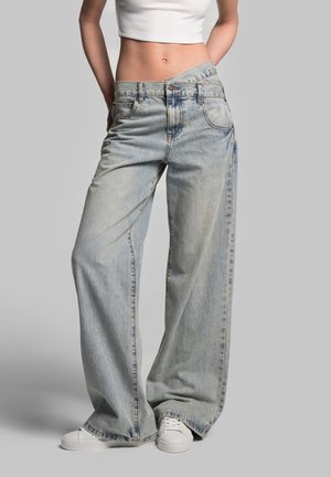 Light blue wide-leg jeans made of denim, featuring a high waist, five pockets, and subtle faded detailing. Paired with white sneakers.