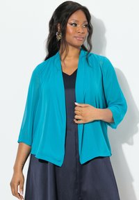 Teal, kevyt kimono-tyylinen jakku, jossa on ¾ hihat, avonainen etuosa ja virtaava muotoilu, käytetty tummansinisen mekon päällä.