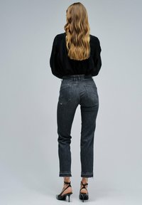 Blusa negra de manga larga combinada con jeans de mezclilla negros de cintura alta y desgastados, con dobladillo deshilachado y dos bolsillos traseros, usados con tacones negros.
