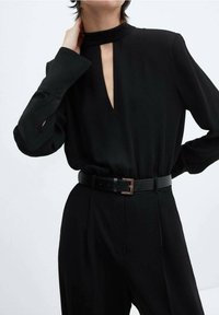 Combinaison noire à manches longues, d�écolleté en keyhole et taille ceinturée. Présente un tissu lisse et une coupe structurée, mettant en valeur l'élégance.