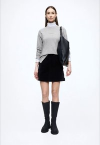 Szara koszula z długim rękawem i stójką, czarna spódnica z sztruksu, czarne kozaki do kolan oraz duża czarna torba typu tote. Prosty, nowoczesny design.